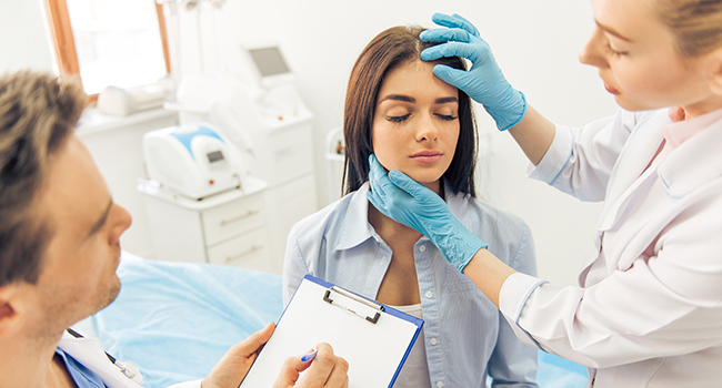 Médico y enfermera revisando la cabeza y cuello de paciente.